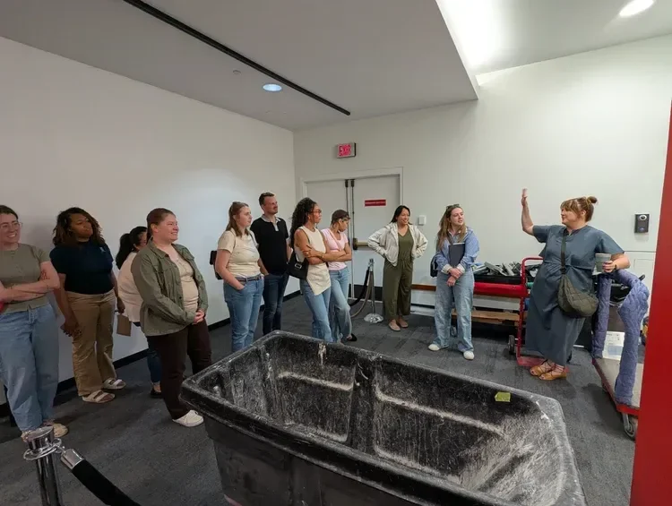 Group of people gathered around a large black industrial tub in a brightly lit room
