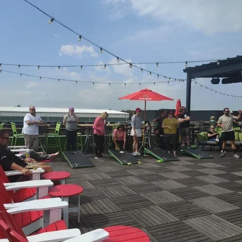 People playing mini golf on a rooftop patio with string lights, red umbrellas, and outdoor seating