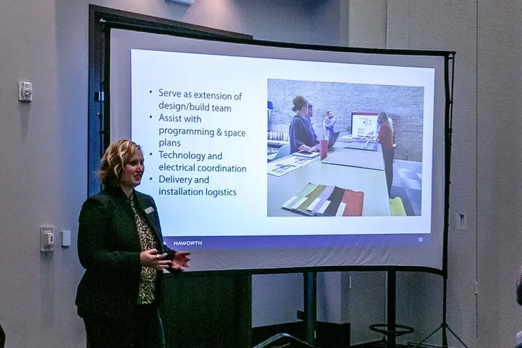 Woman presenting a Haworth office design and logistics slide on a projection screen