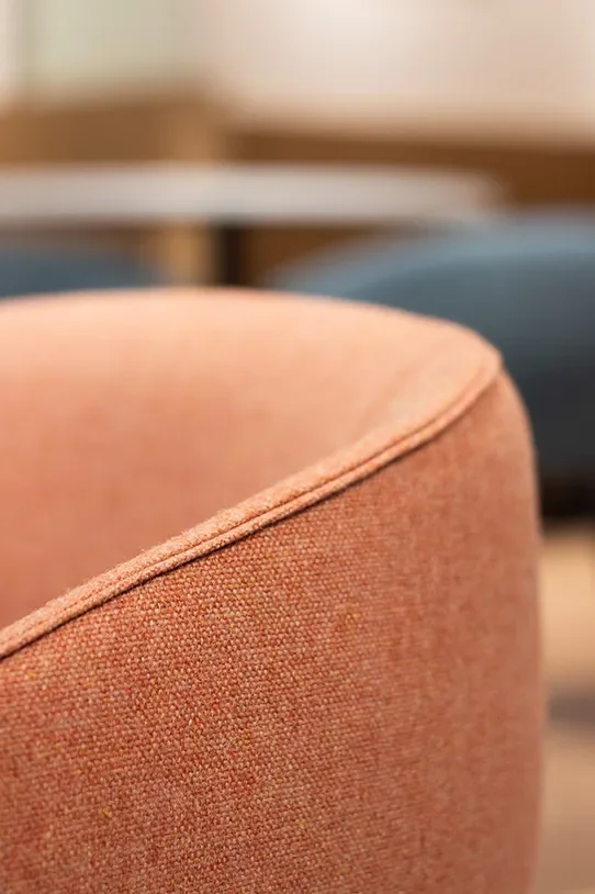 Close-up of a terracotta-colored upholstered sofa or armchair with visible fabric texture and piping