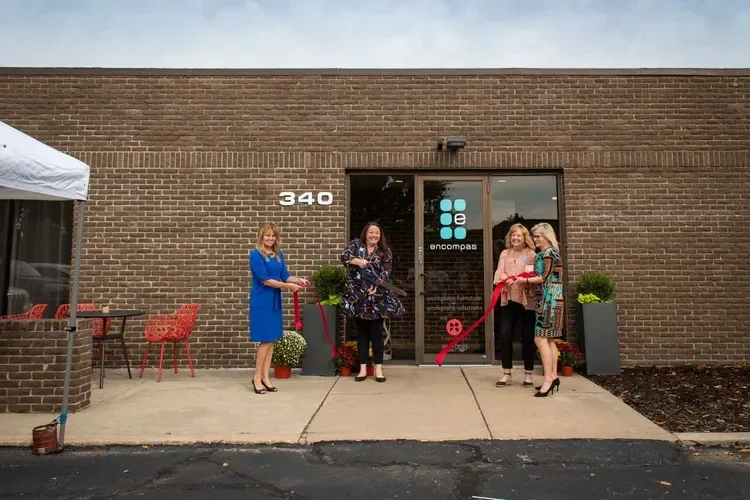 Four women cut a red ribbon outside the Encompass workspace at 340 during a grand opening ceremony.