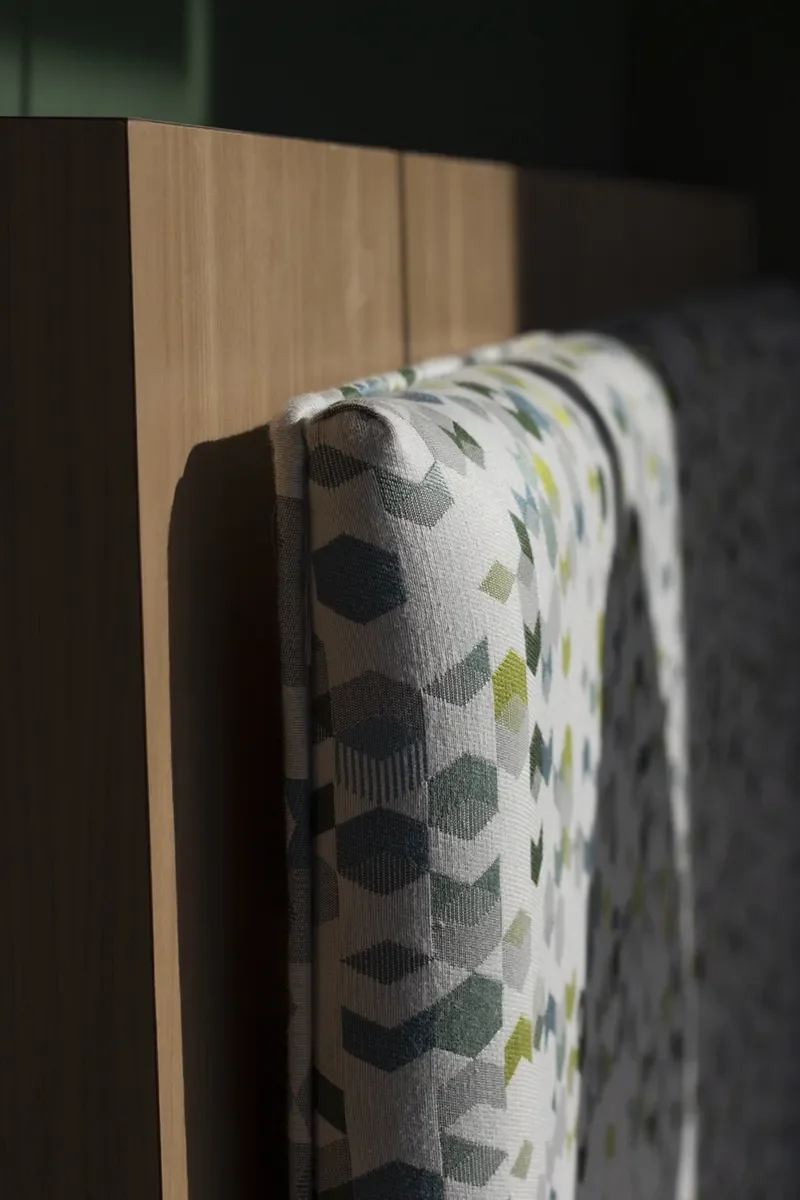 Close-up of a patterned upholstered chair with geometric green and gray fabric beside a wooden panel.