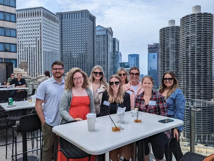 Group of coworkers posing on a rooftop patio with drinks and a Chicago skyline featuring Marina City towers