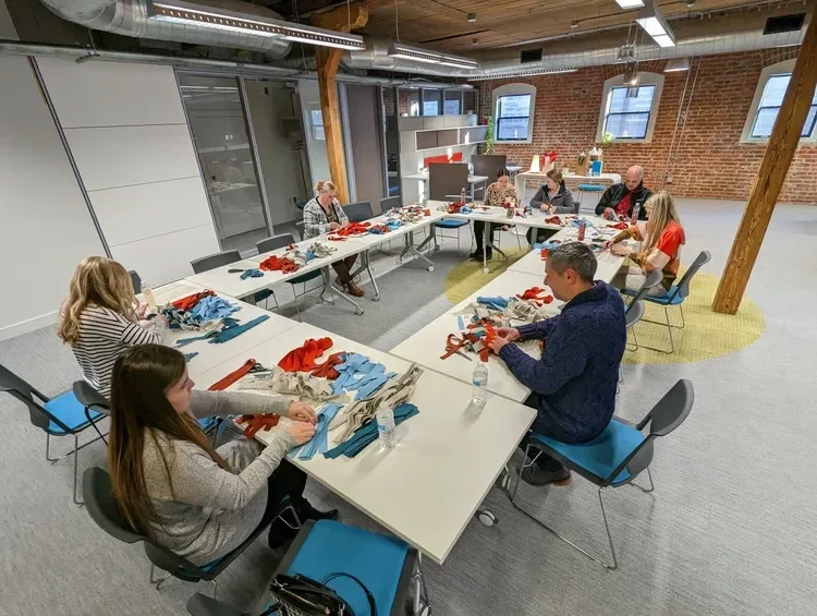 Group of people assembling colorful fabric materials around tables in a bright industrial-style workshop