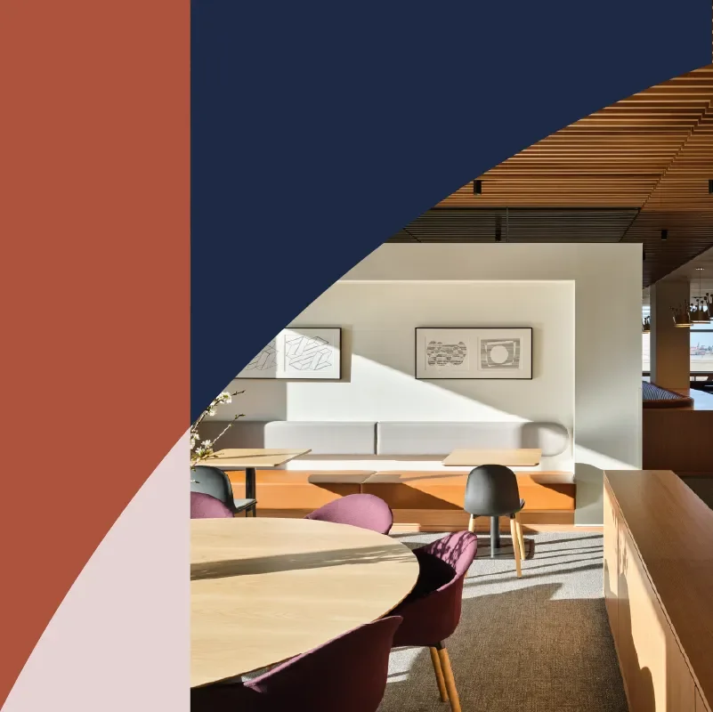 Modern restaurant interior with wood-paneled ceiling, white banquette seating, round tables, and burgundy chairs framed by abstract geometric shapes