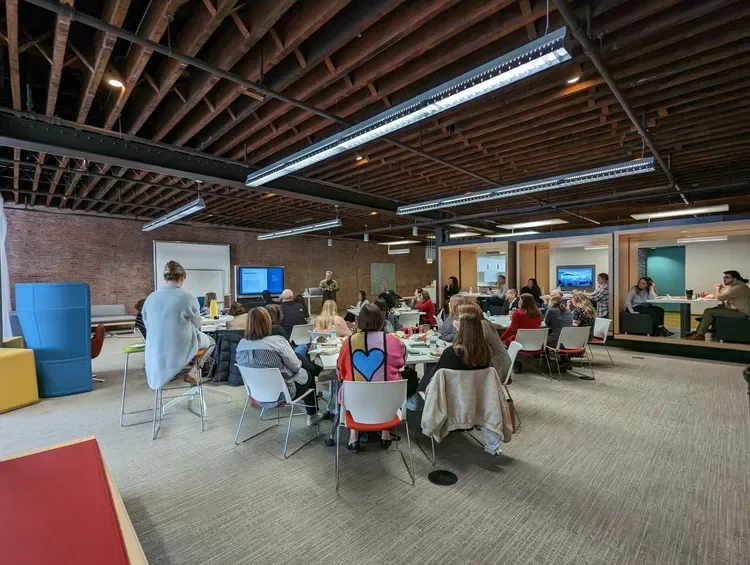 Collaborative office meeting with employees seated around tables in an industrial-style workspace