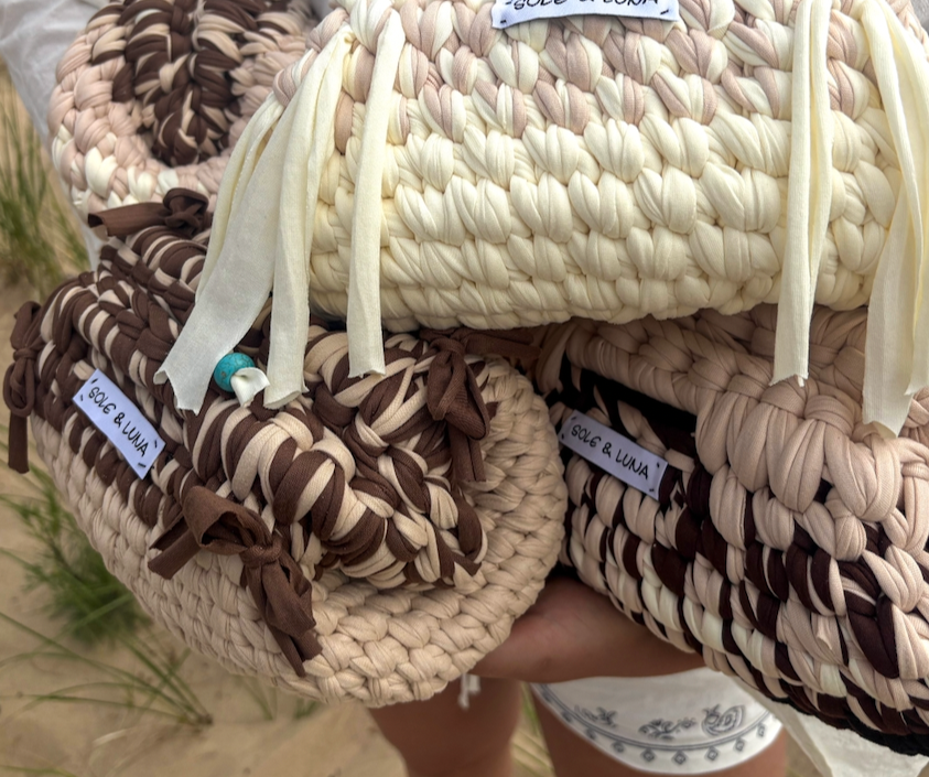 Stacked woven handbags in beige, brown, and cream with tags labeled "VICA & LUNA" and tied with fabric straps, held by a person outdoors.