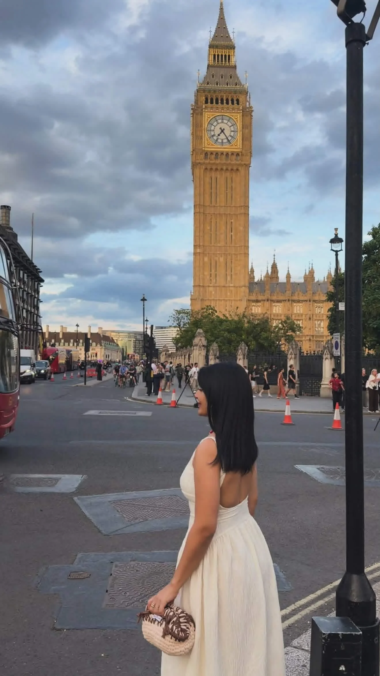 A woman in a white dress walking on a city street with Big Ben clock tower and the Houses of Parliament in London in the background.