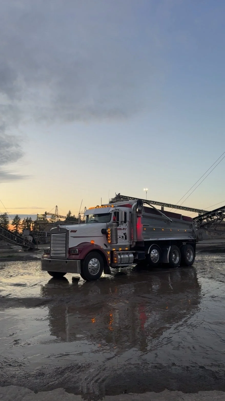 A large white and red truck parked on wet ground at dusk with a partly cloudy sky.