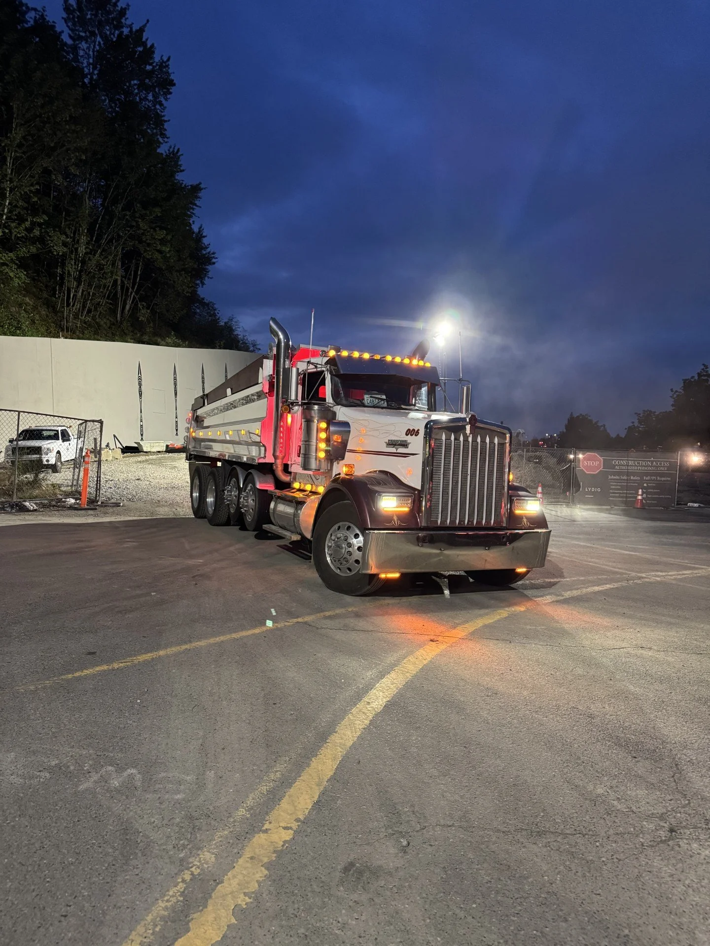 A large semi-truck parked in a lot at dusk with dark clouds overhead, a fence, and a sign that reads 'Construction Access' in the background.