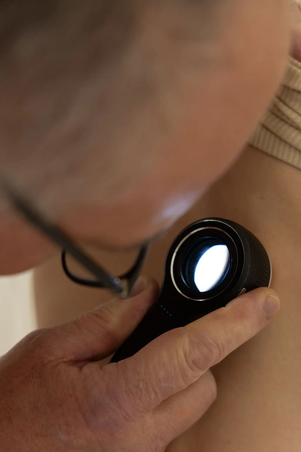 Person using a flashlight or black light on their skin, with part of their face and arm visible.