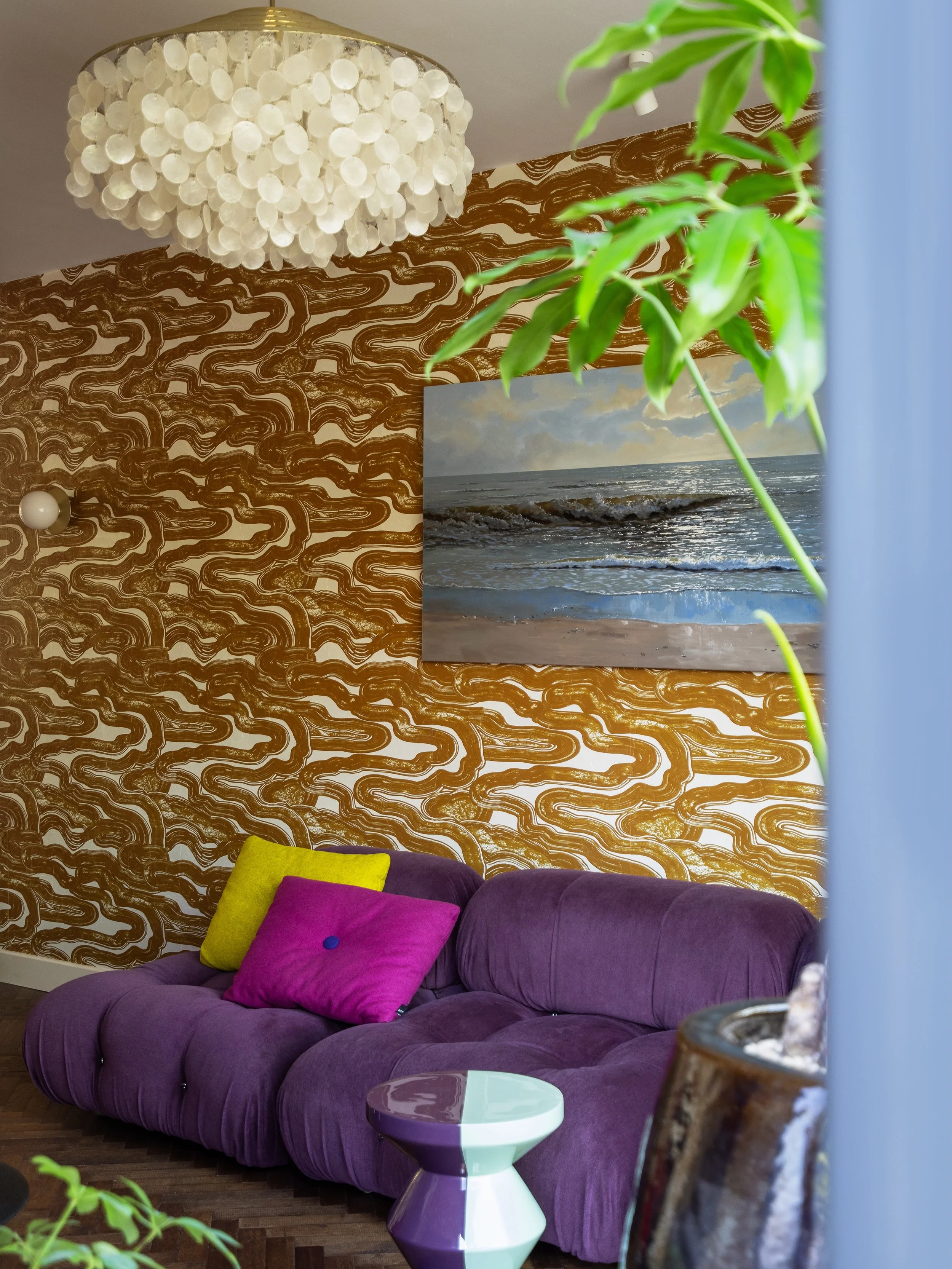RIDE THE WAVE ~ Vlak achter het strand mag de zee ook binnen komen. Het golvende behang, de schelpen hanglamp en het schilderij van de kust zijn knipoogjes naar het strandleven. Een plek om samen tv te kijken of lekker weg te zakken. Swipe ➡️ om te z