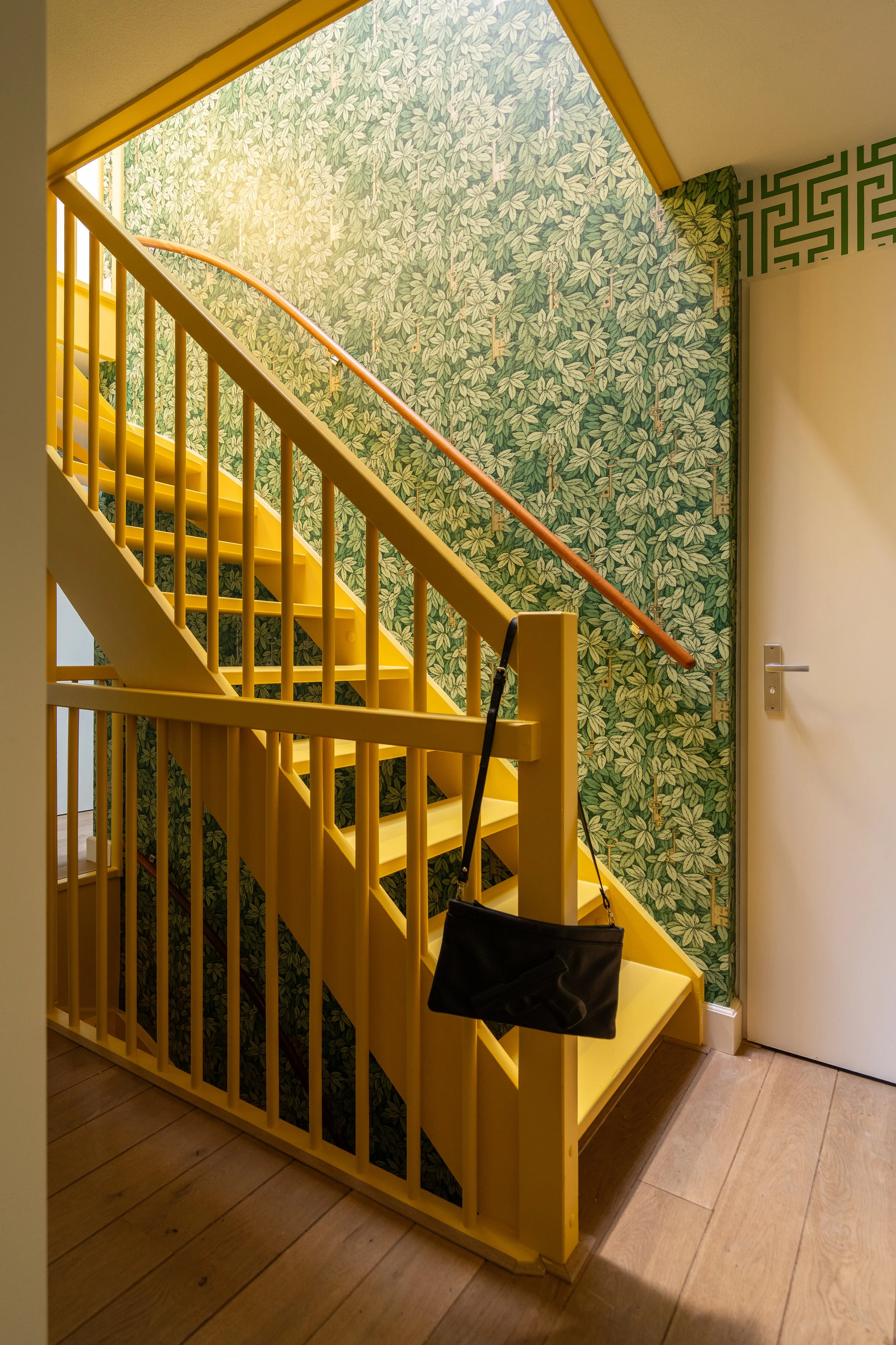 Zonnig trapgat geverfd in een warme gele kleur van Little Greene en een plafondhoog groen botanisch behang van Cole & Son na een renovatie.