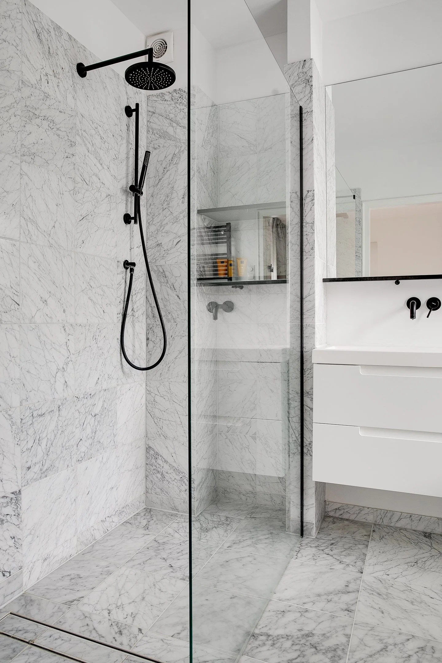 Douche en op maat gemaakte spiegel over de gehele wand boven wastafel in luxe, marmeren badkamer, optisch vergrotend effect.