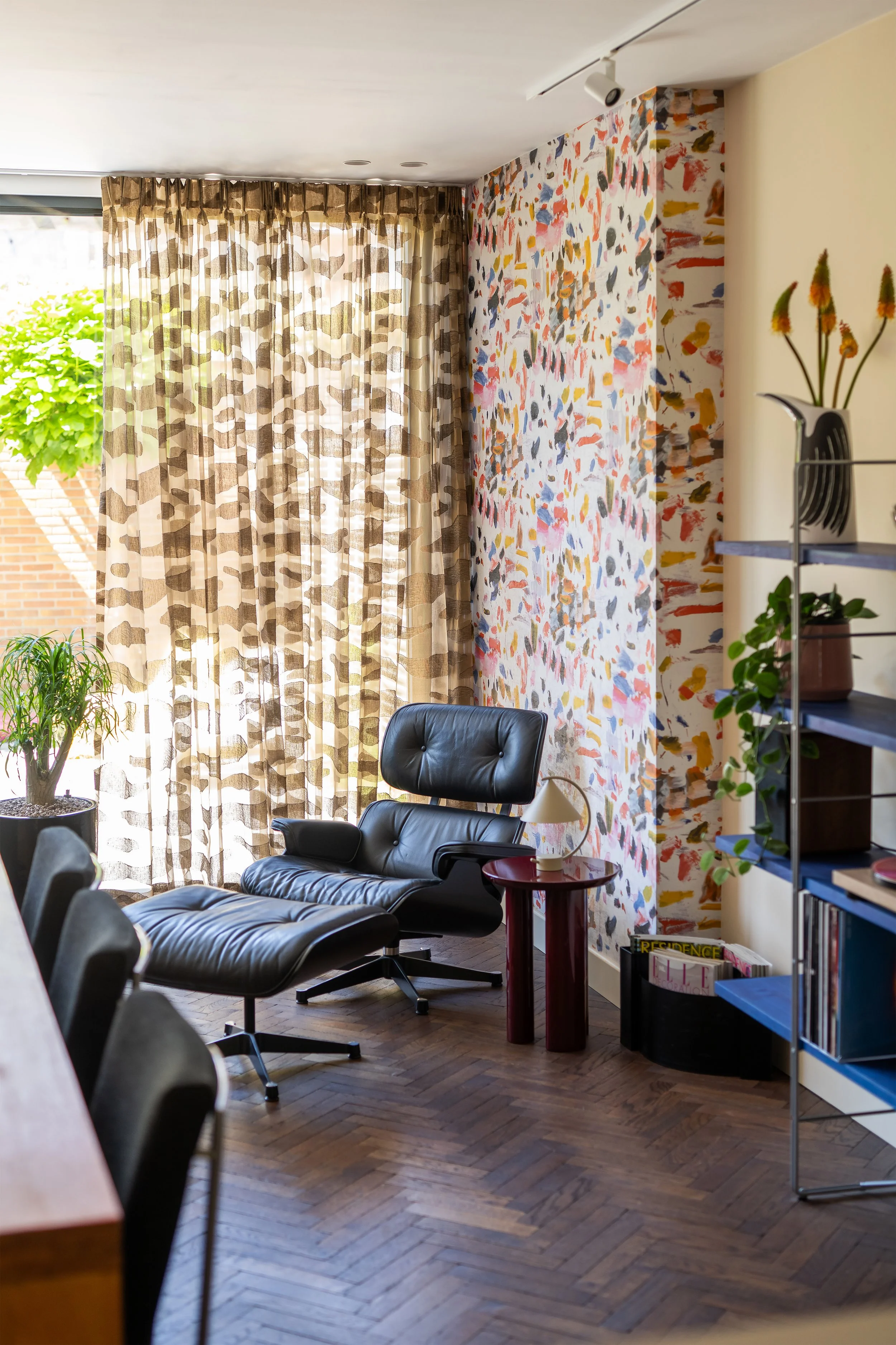 Luxe woonkamer zithoek met een mid-century Vitra Eames Lounge Chair, &Tradition bijzettafel en kleurrijk Pierre Frey behang.