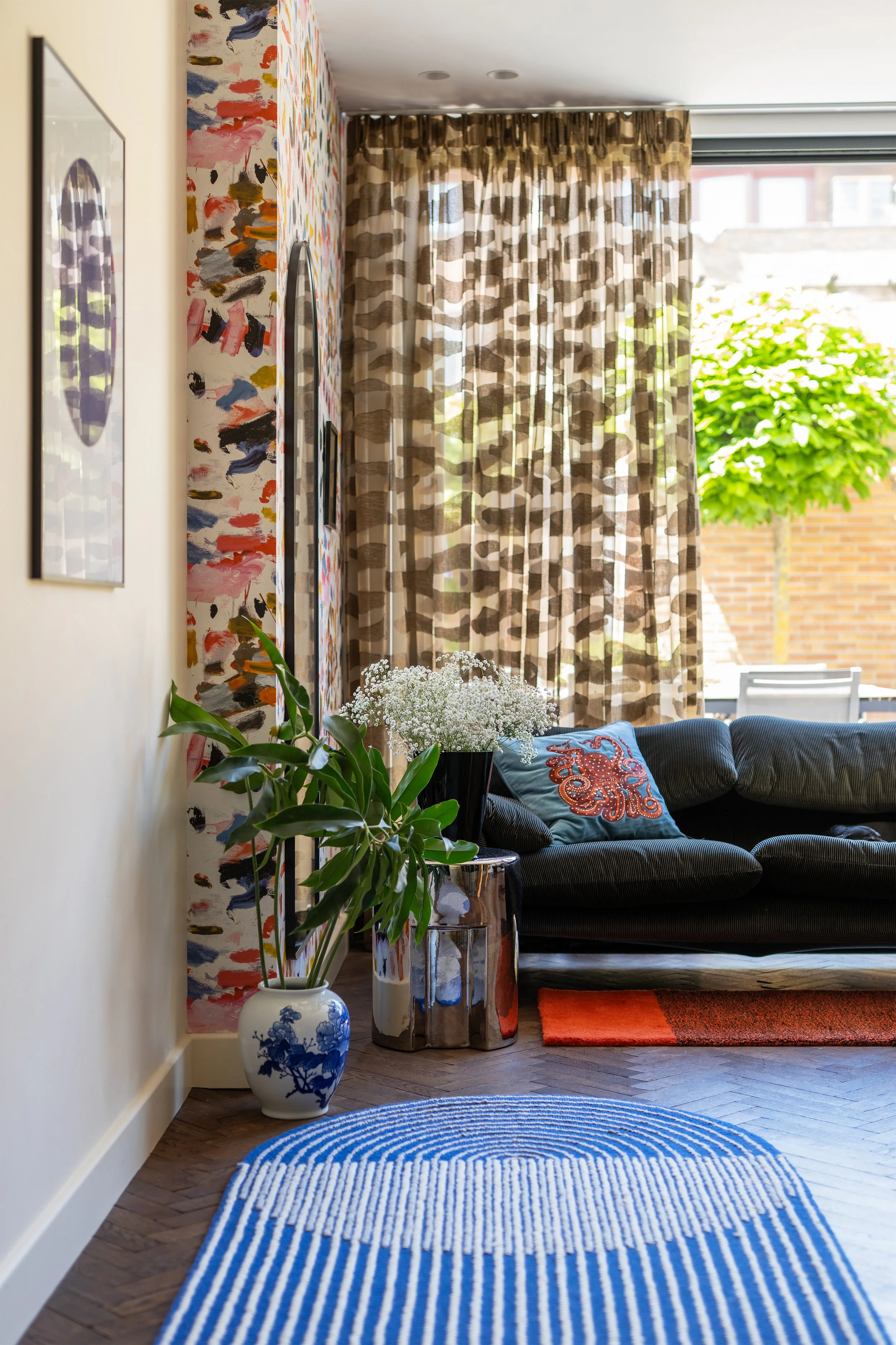 Lichte aanbouw met slanke stalen schuifpui, golvende Kendix Ameba inbetween gordijnen, blauw gestreept vloerkleed van Gan Rugs by MUT Design en Pierre Frey behang.