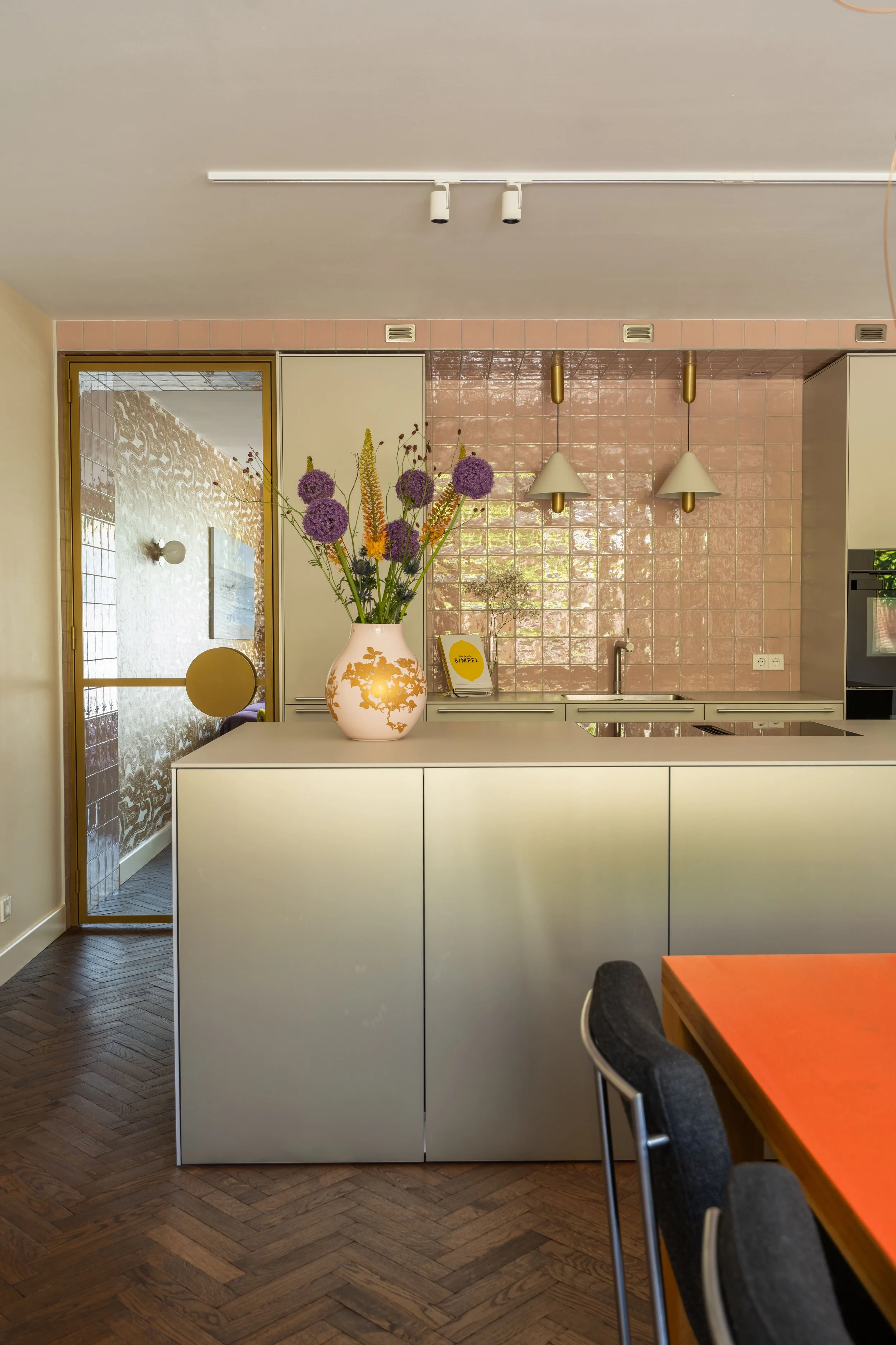 Eclectisch interieurontwerp van een luxe keuken met roze wandtegels, gouden designdetails en maatwerk stalen deuren met ronde handgrepen in een gerenoveerde nieuwbouwwoning.