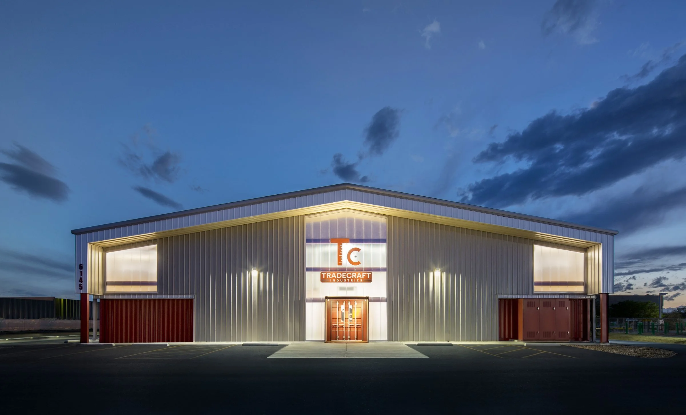 The gabled metal building at night, with the illuminated entry bay set into the container base.