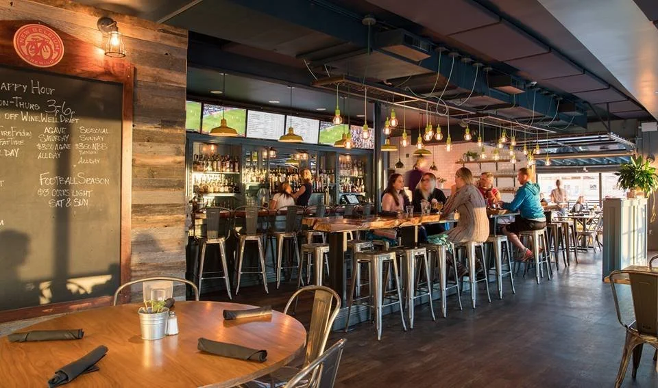 Reclaimed wood walls, a chalkboard menu, and the bar beyond — the pub on a busy afternoon.