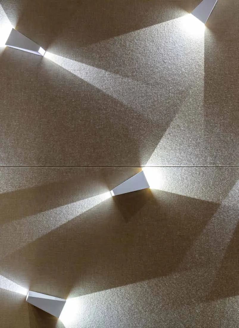 Angled fixtures cast overlapping triangles of light across the faceted felt wall.