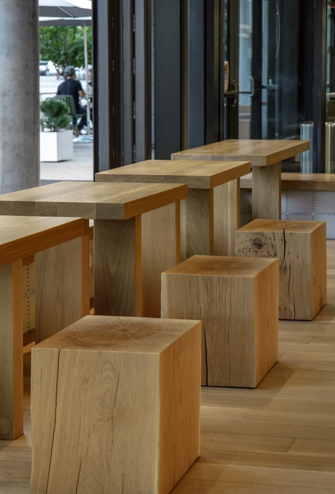 Oak block stools and counter-height tables line the glazed facade.