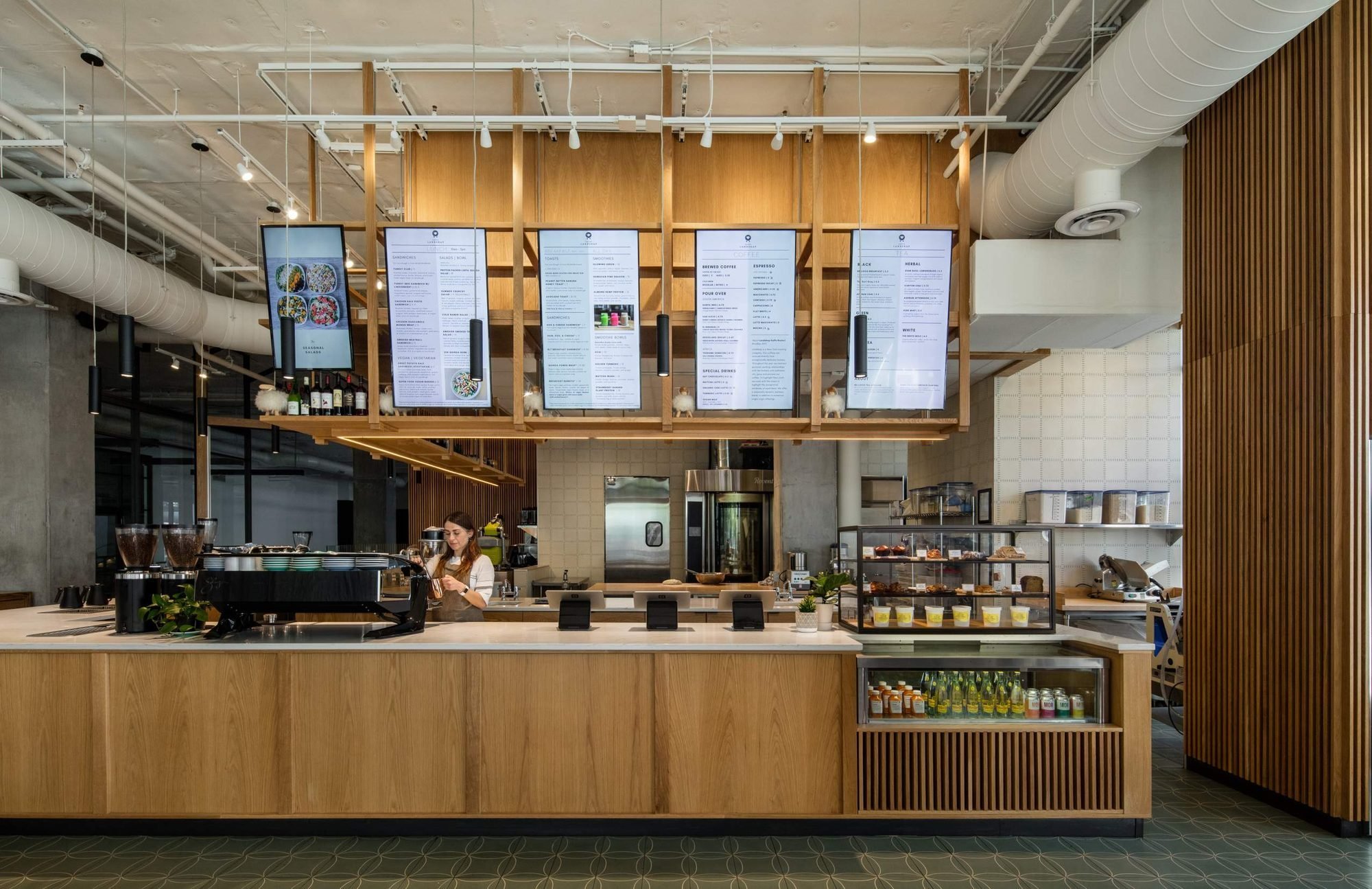 The white oak service counter sits beneath the shelving canopy, pastry case to one side.
