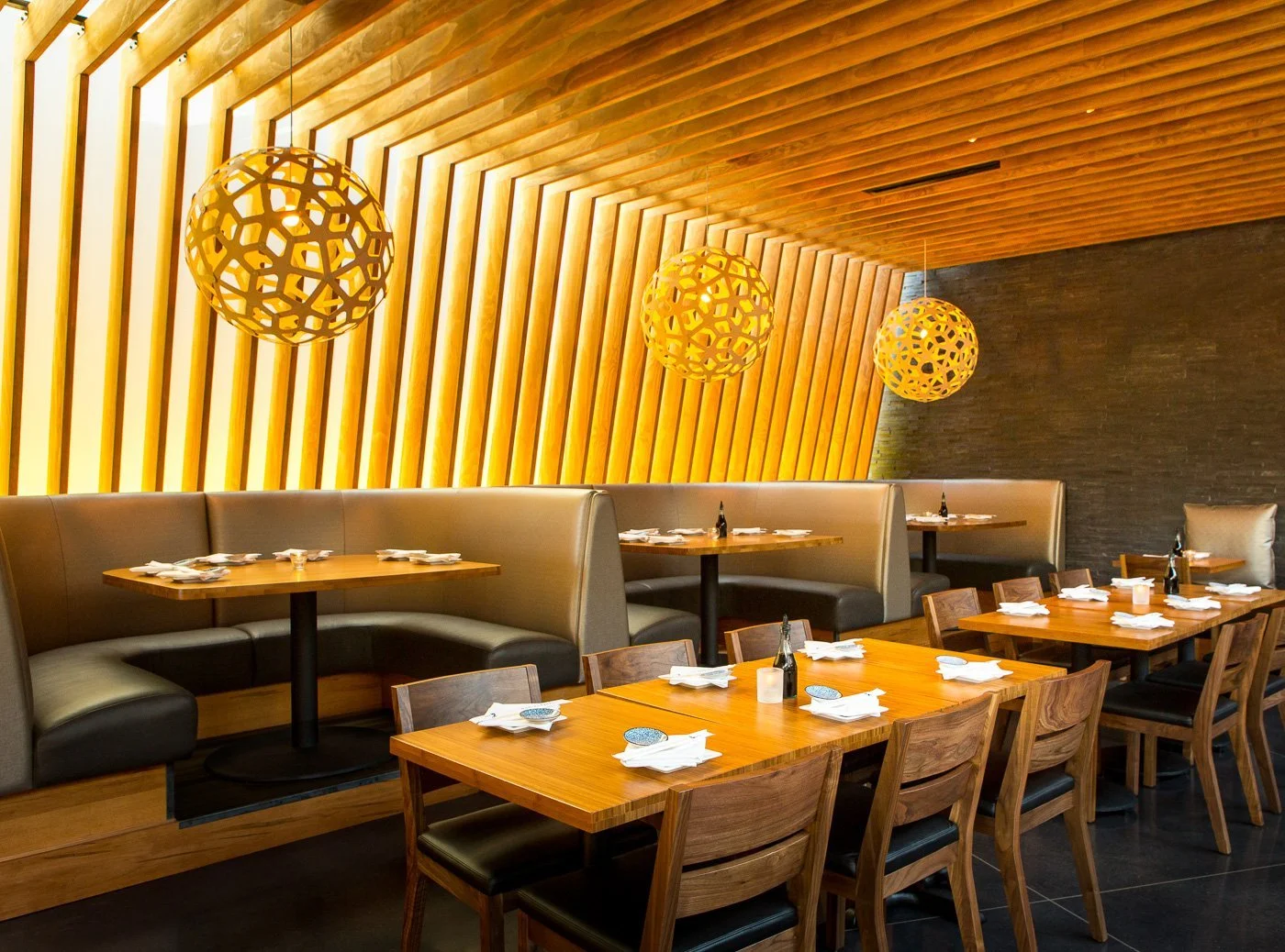 Woven pendants hang from the slatted ceiling over banquette dining.
