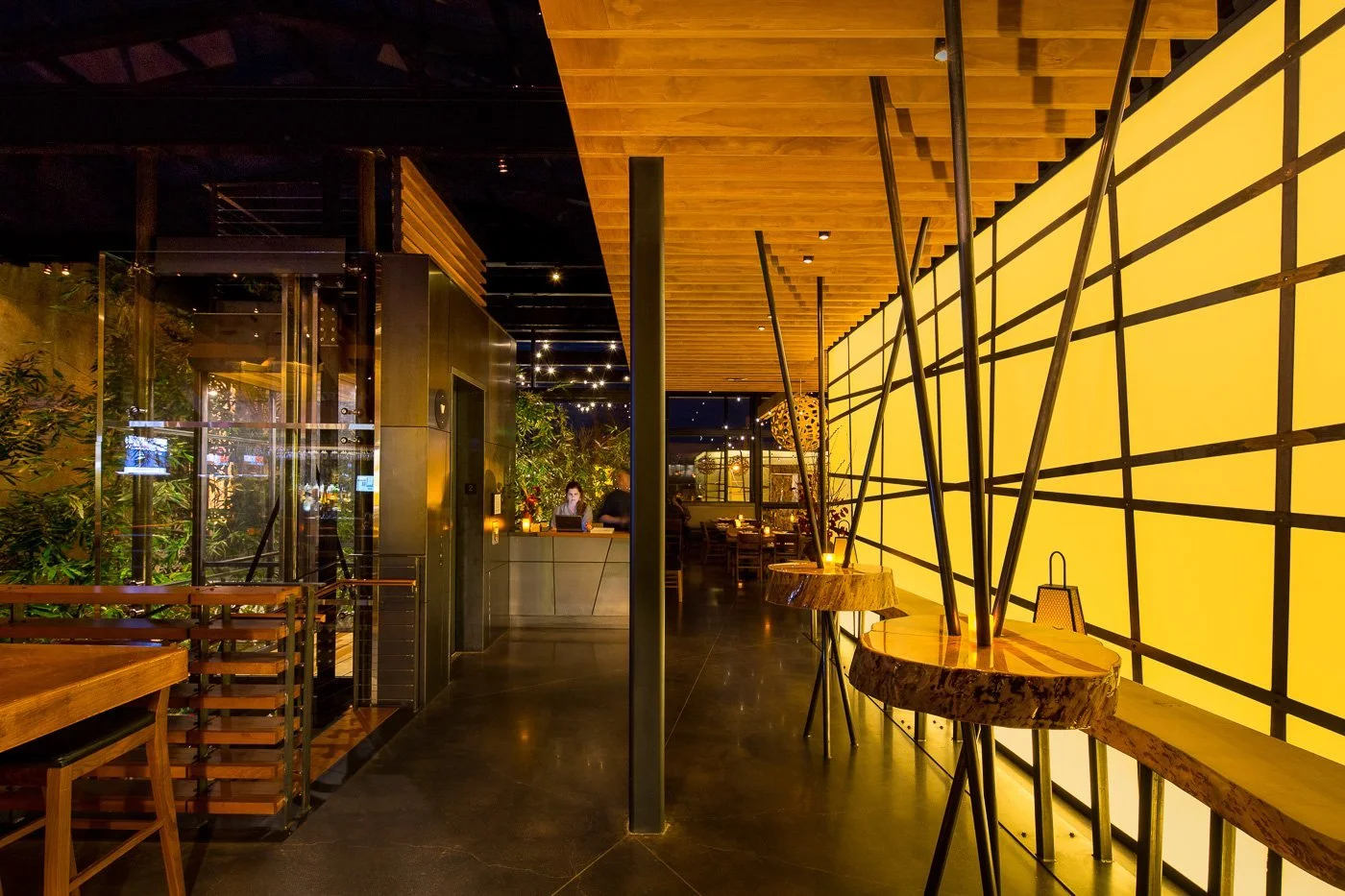 A backlit yellow wall with a black lattice reads like a shoji screen along the upper dining room.