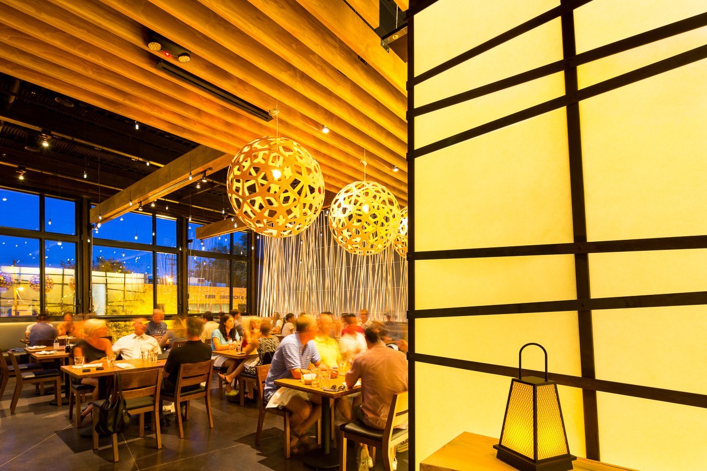 Woven pendants over the upper dining room, the lattice wall glowing behind.