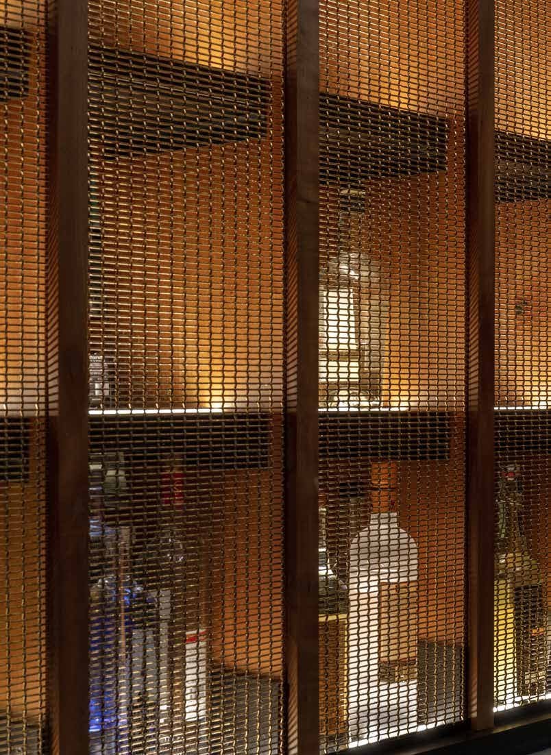Detail of the bronze mesh and cherry screen, backlit bottles behind.