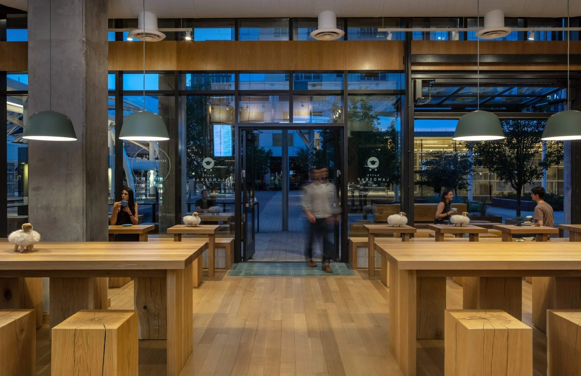 The café in the evening, communal tables and sage pendants under a darkening sky.