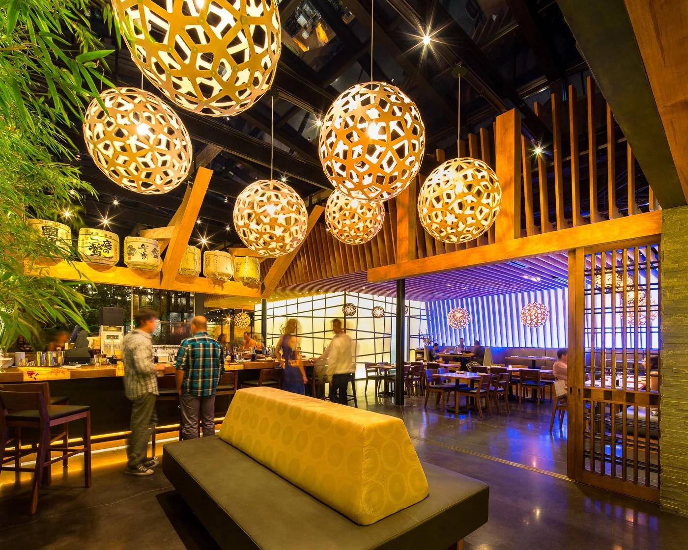 Woven globe pendants cluster over the lounge, the open kitchen lit beyond.