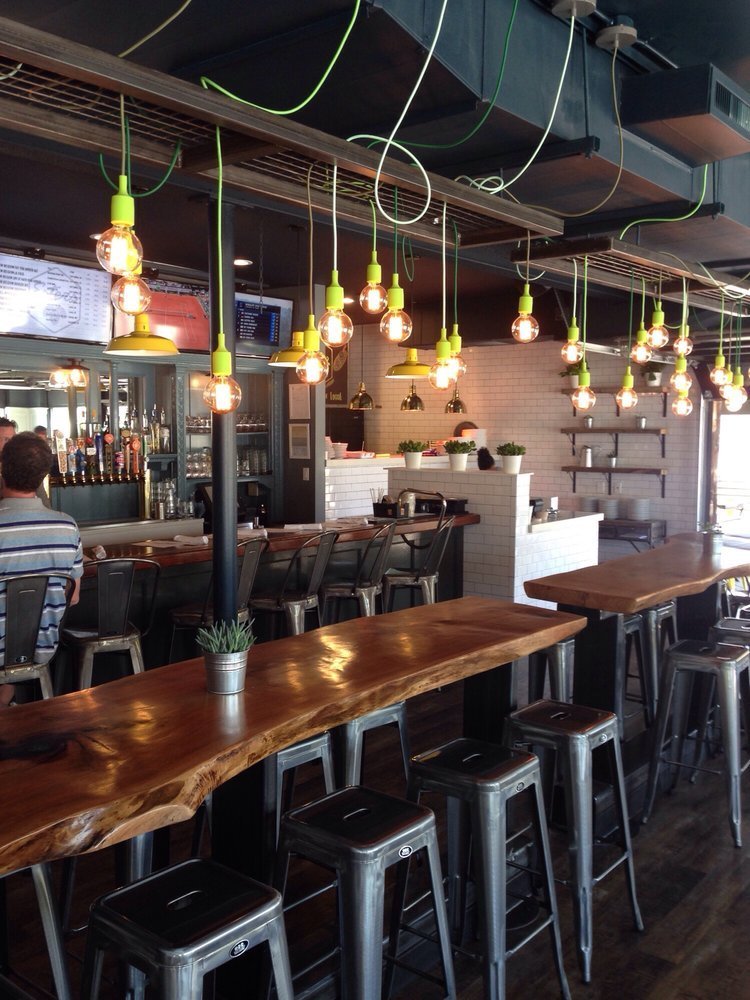 Bare-bulb pendants on banana-yellow cords hang over the bar and a live-edge communal table.