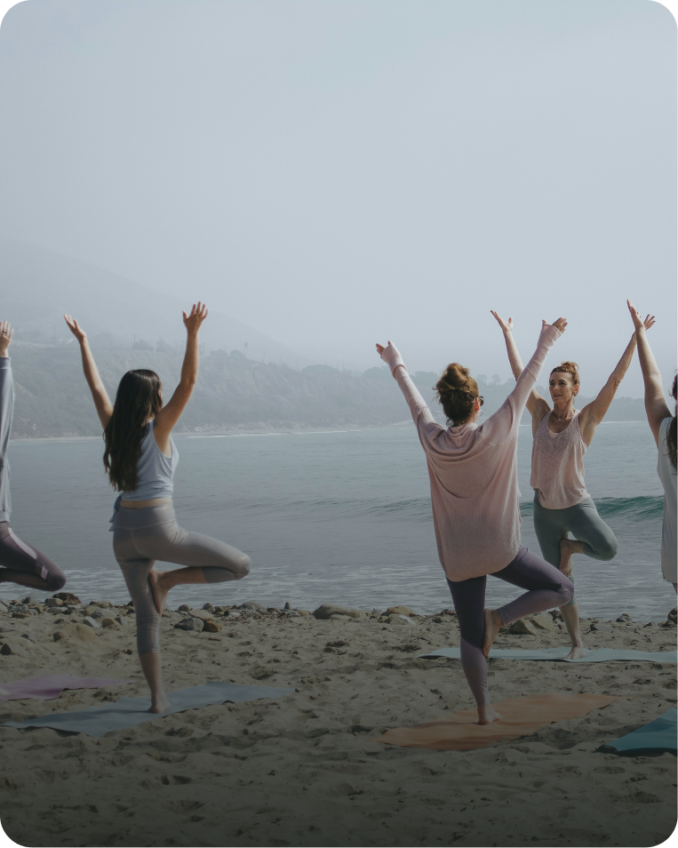 People practicing yoga on a beach by the water during daytime.