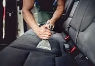 Person vacuuming a car seat with a handheld vacuum cleaner.