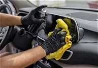 Person cleaning a car's dashboard with a yellow cloth.