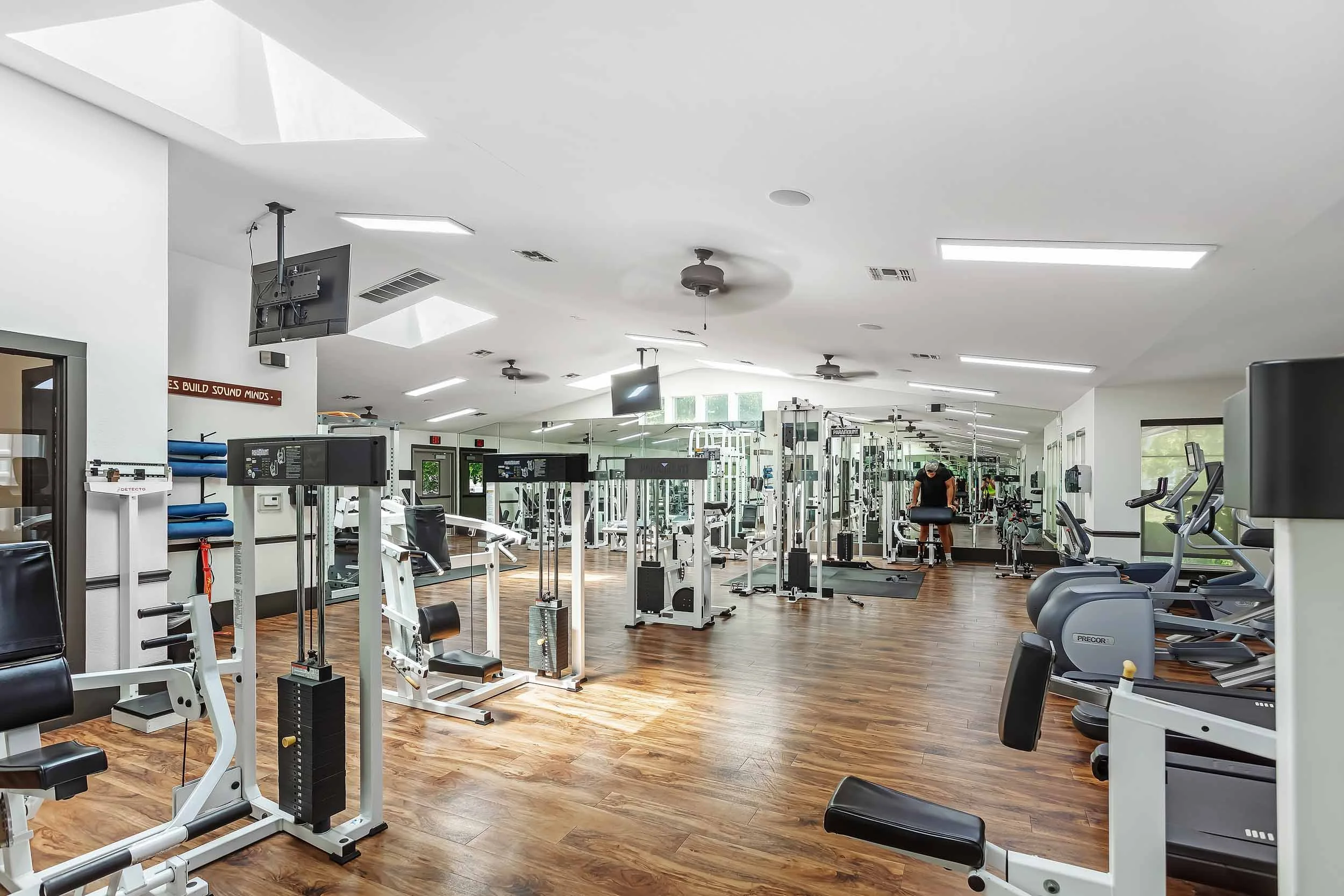 Interior of a modern gym with exercise equipment, mirrors, and a person working out.