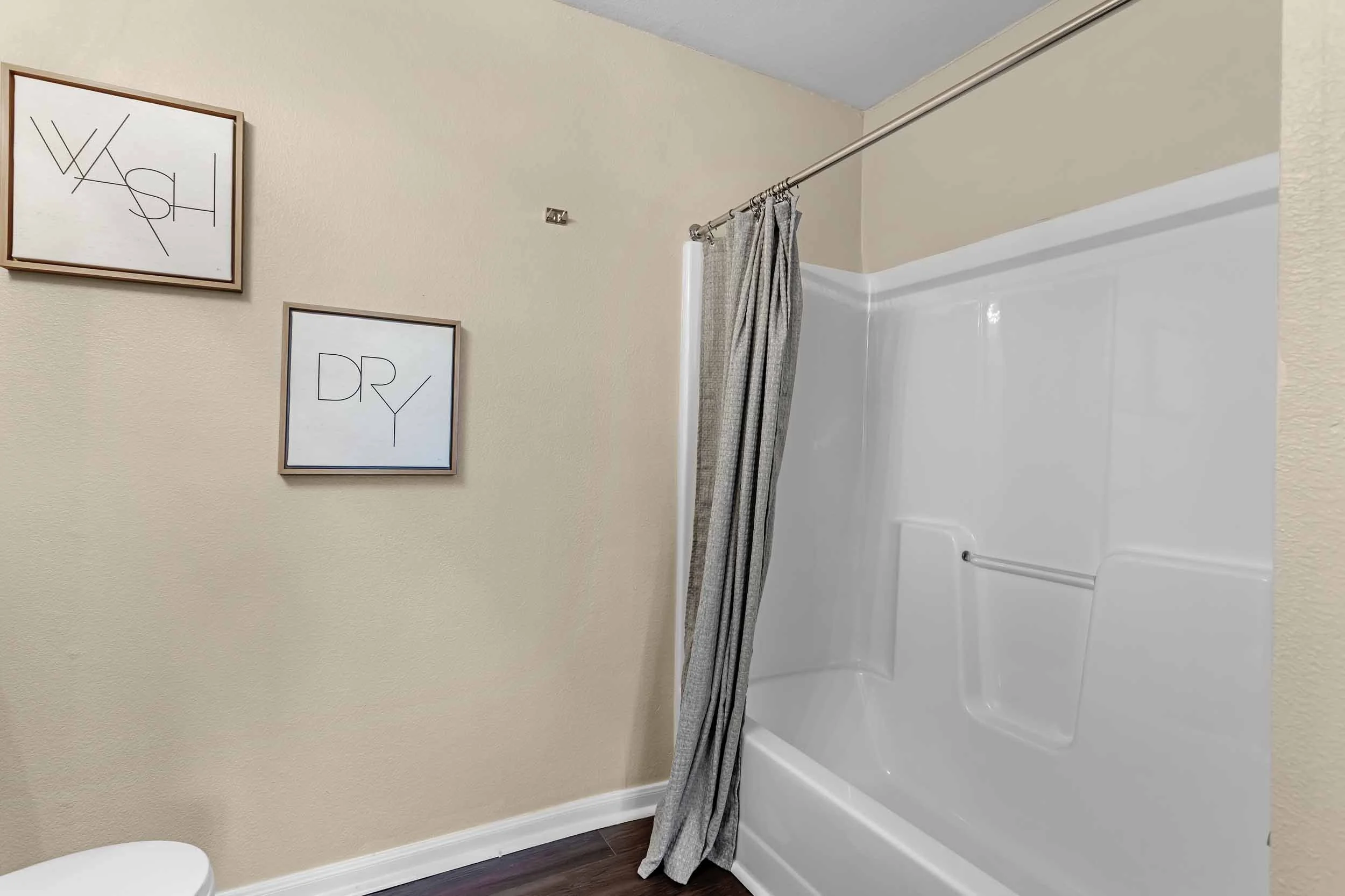 Bathroom with shower, beige walls, framed artwork, and a toilet.