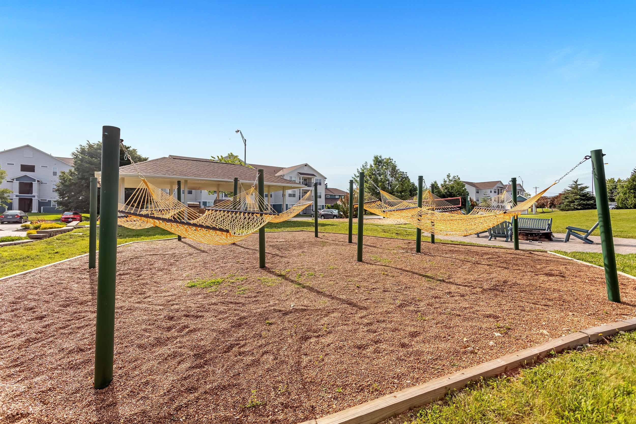 Playground with hammocks, surrounded by houses and green trees, under a clear blue sky.