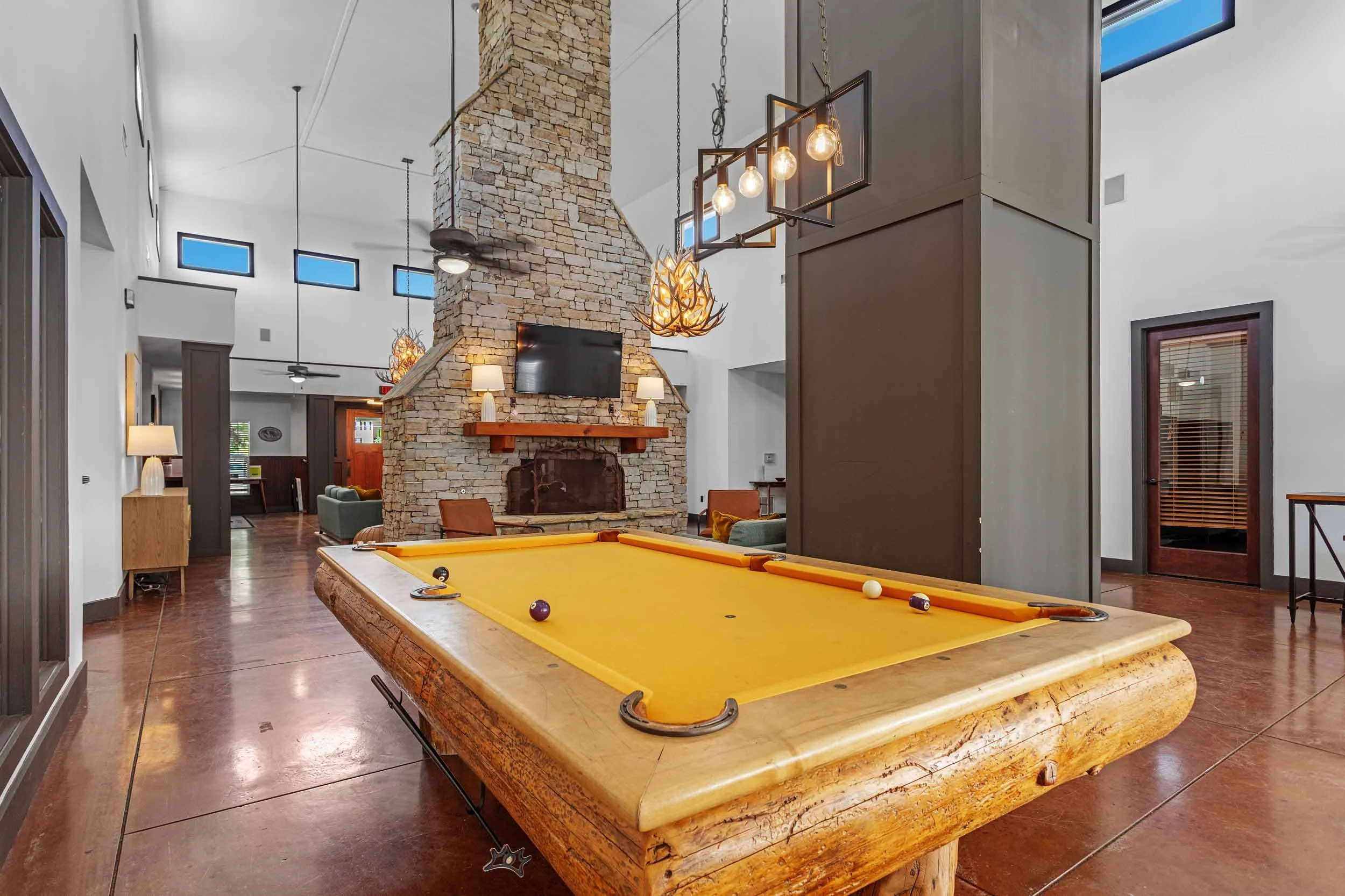 Interior of a recreational room with a yellow pool table, a stone fireplace with a mounted TV, and modern lighting fixtures.