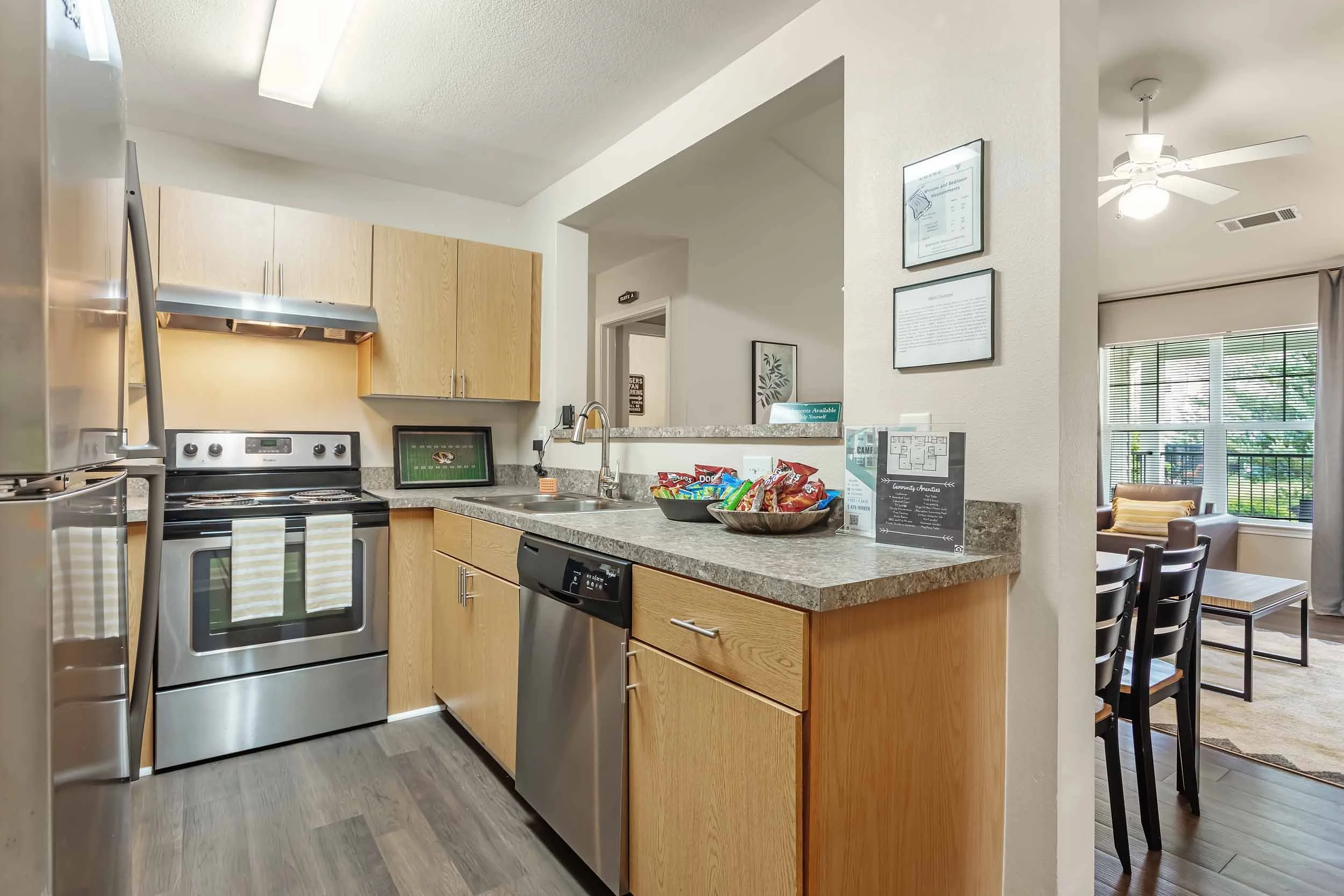 A modern kitchen with light wood cabinets, stainless steel appliances, a granite countertop, and a separate dining area with chairs and large windows.