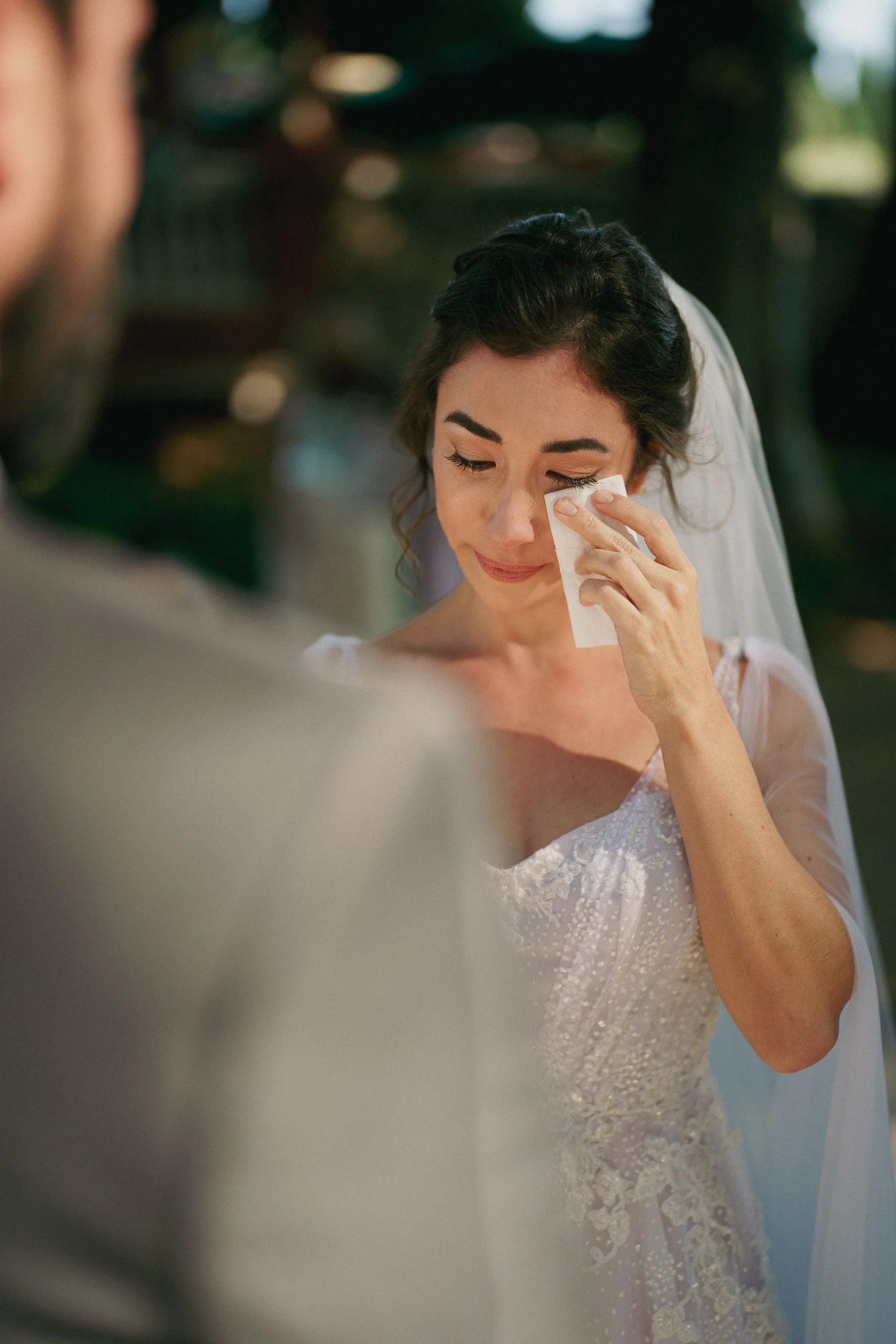 A woman in a wedding dress wiping away tears with a tissue.