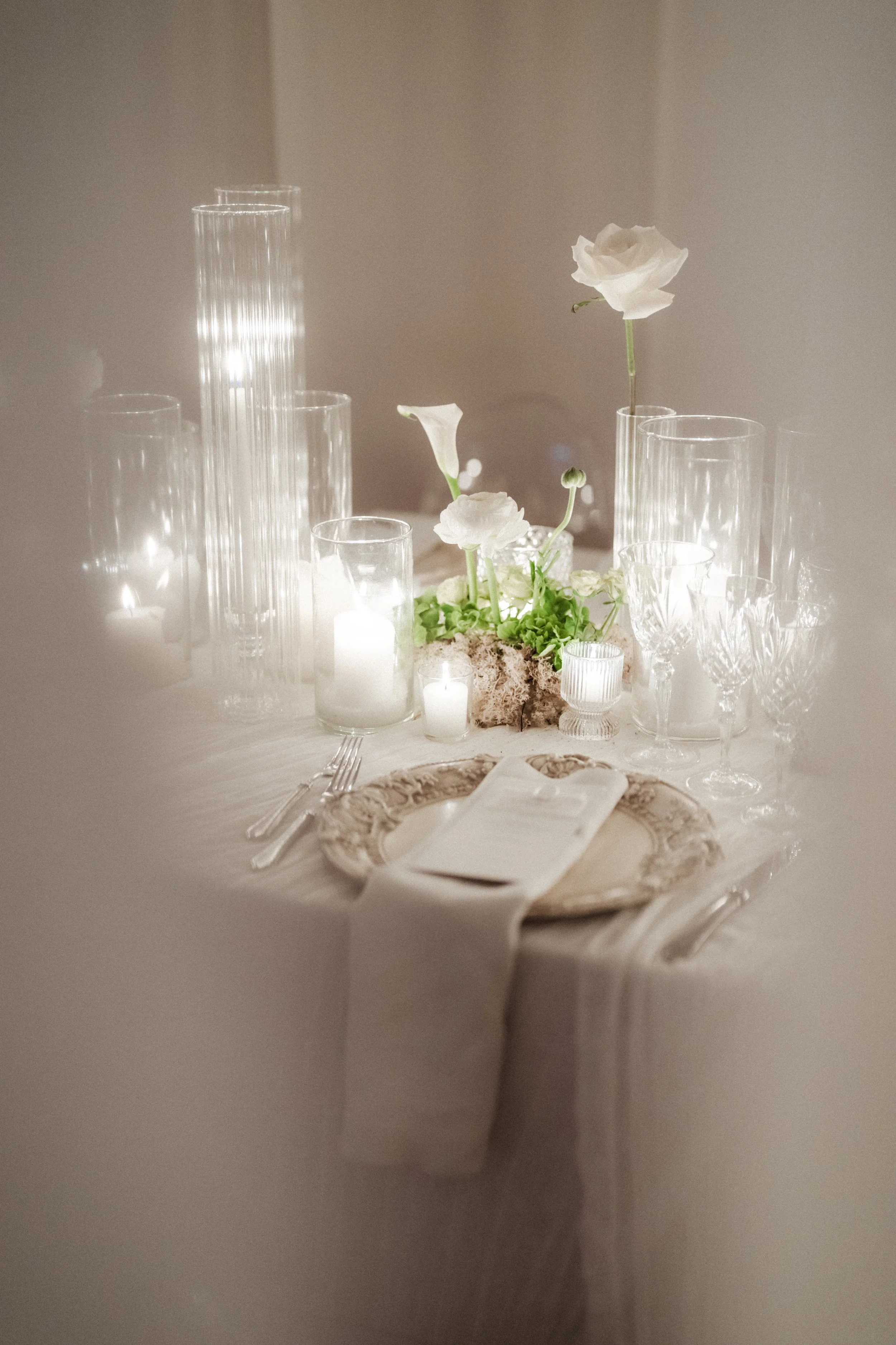 Elegant table setting with white flowers in vases, candles, and glassware on a white tablecloth.