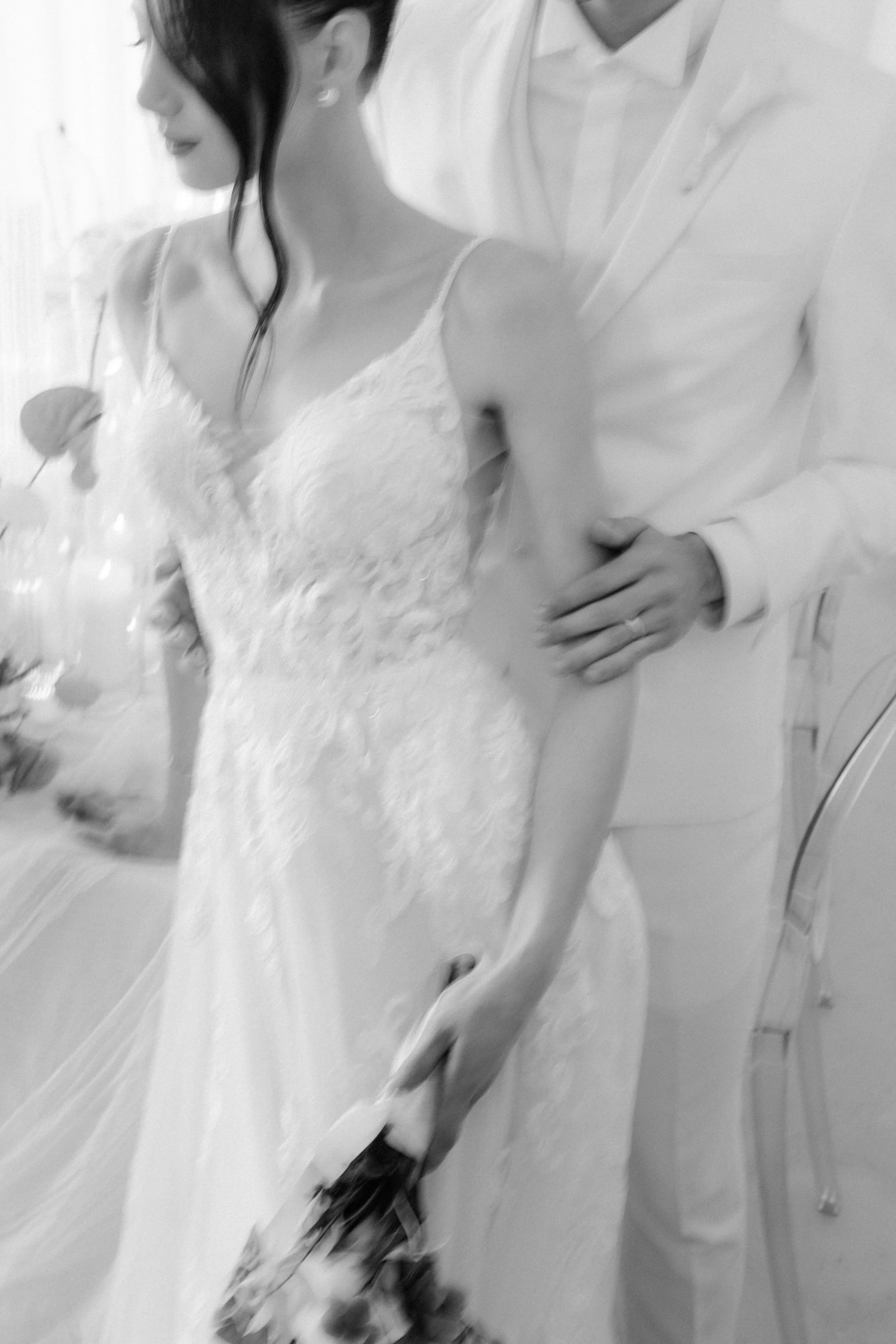 A glass of red wine held by a person wearing a wedding dress, with another person in a suit standing close nearby, possibly at a wedding or formal event.