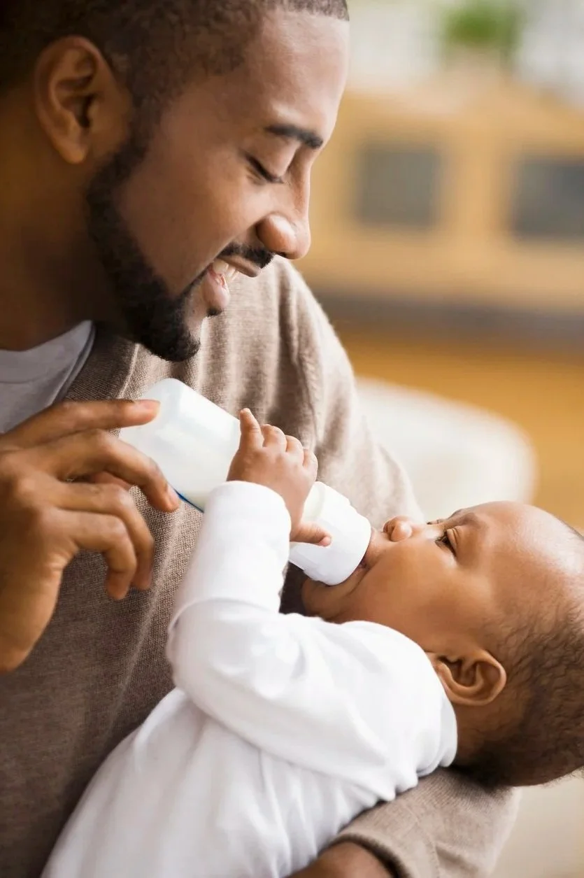 A father smiles as he feeds a baby with a bottle. The baby and father have been participating in infant feeding therapy in Lemont, IL.