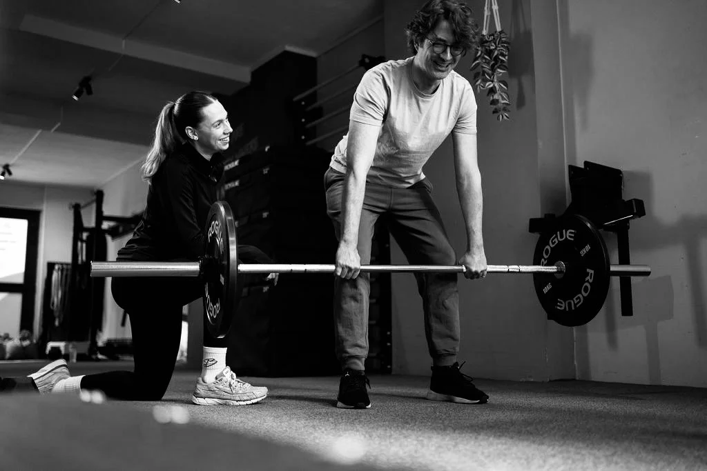 Een man tilt gewichten terwijl een vrouw hem begeleidt in een sportschool.