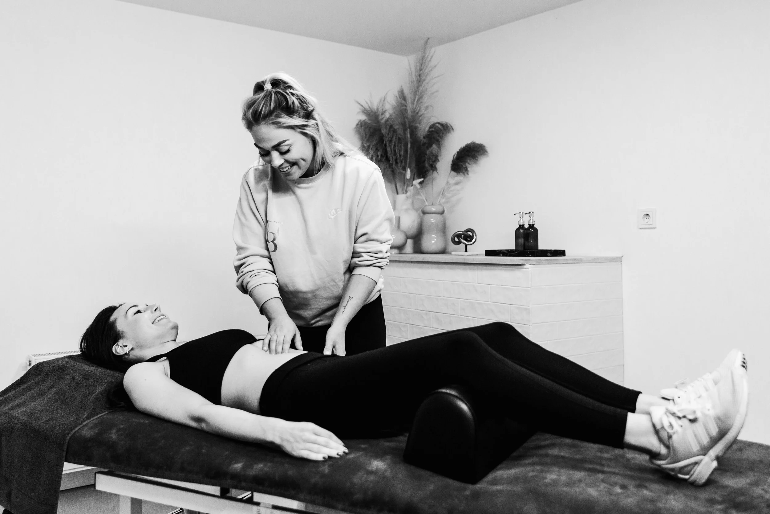 Vrouw ligt op een behandeltafel en krijgt een schoudermassage van een masseur in een kuuroord of spa-omgeving.