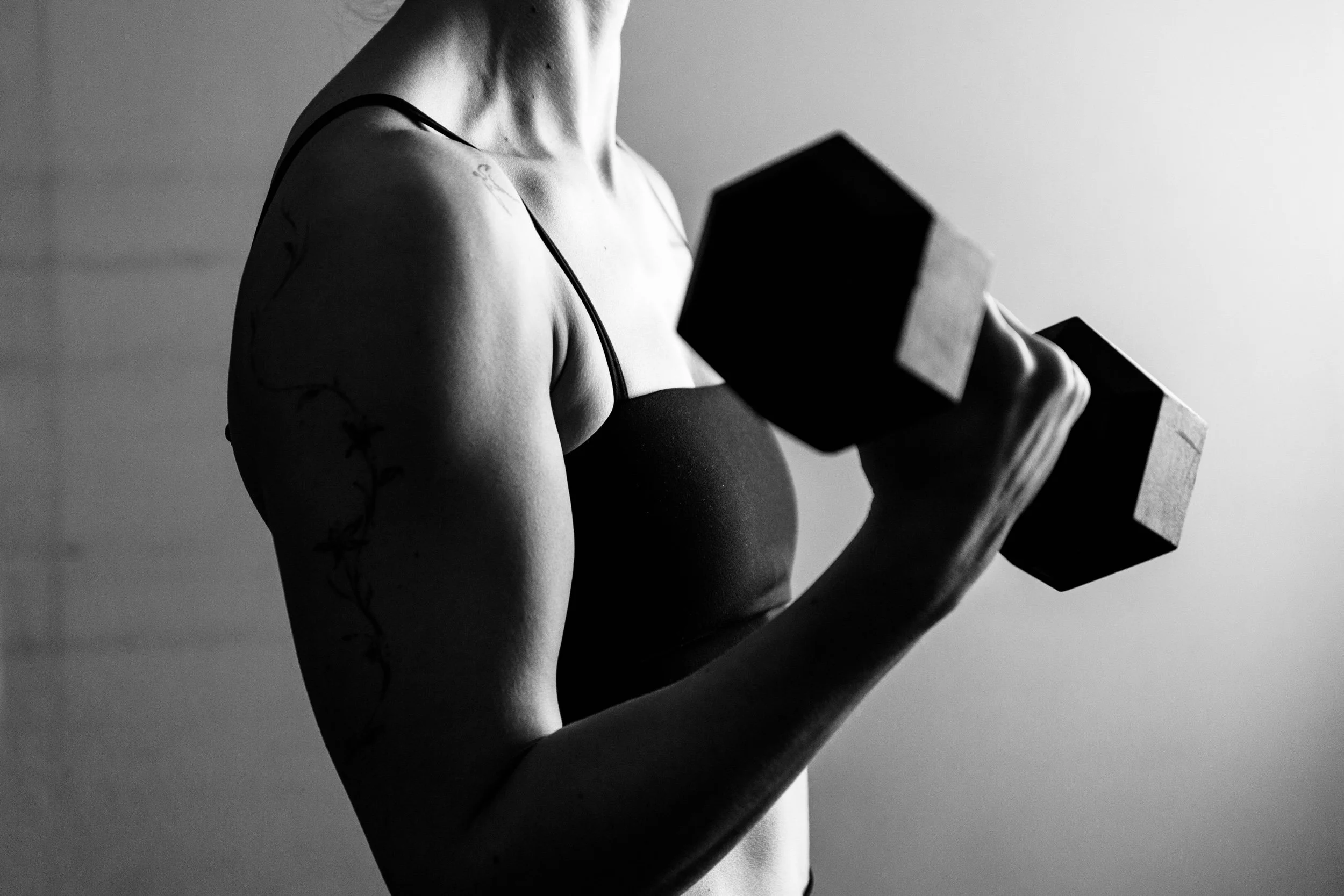 Een zwarte en witte foto van een vrouw die een dumbbell omhoog tilt.