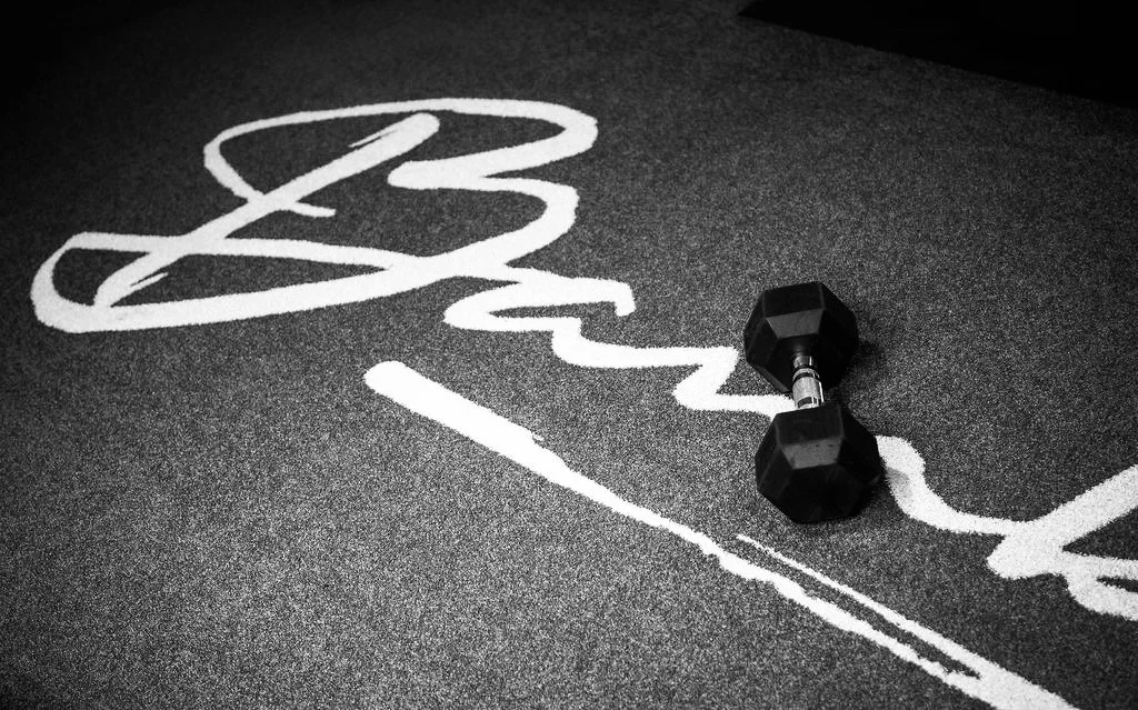 Een zwarthalve sportvloer met witte tekst en een zwart handgewicht. Het woord 'Crossfit' is gedeeltelijk zichtbaar.