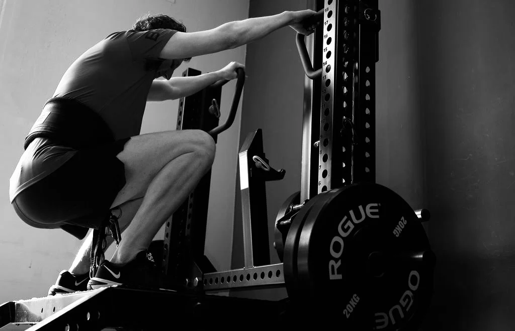 Een persoon die squats doet met een halter op een sportschool.